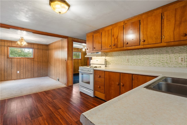 kitchen with dark wood-type flooring, sink, a notable chandelier, white gas stove, and wood walls