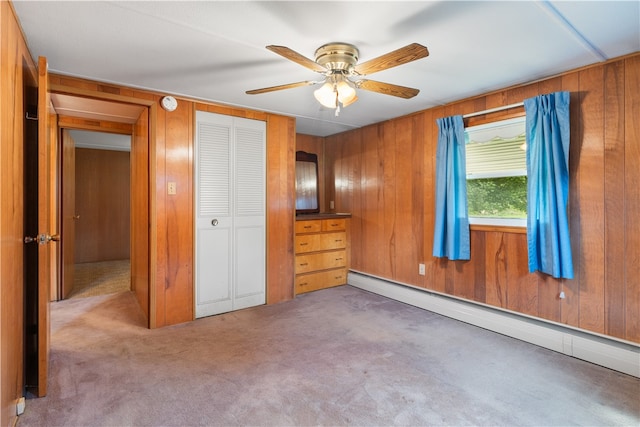 unfurnished bedroom featuring carpet, wooden walls, ceiling fan, a baseboard radiator, and a closet