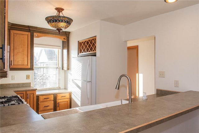 kitchen with kitchen peninsula, sink, decorative light fixtures, and white refrigerator