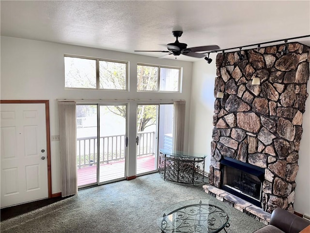 living room featuring carpet flooring, ceiling fan, a stone fireplace, a towering ceiling, and a textured ceiling