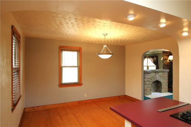 unfurnished dining area featuring wood-type flooring, a textured ceiling, and a stone fireplace