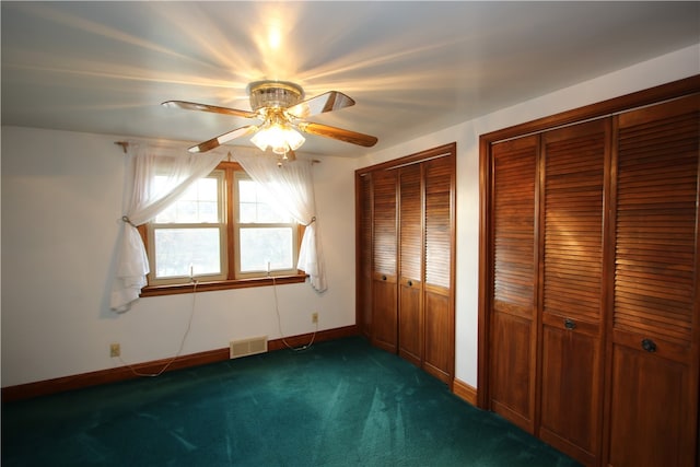 unfurnished bedroom featuring multiple closets, ceiling fan, and dark colored carpet