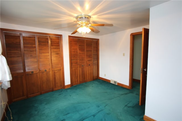 unfurnished bedroom featuring two closets, dark carpet, and ceiling fan