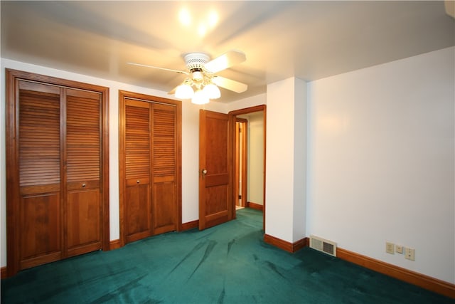 unfurnished bedroom with dark colored carpet, ceiling fan, and multiple closets