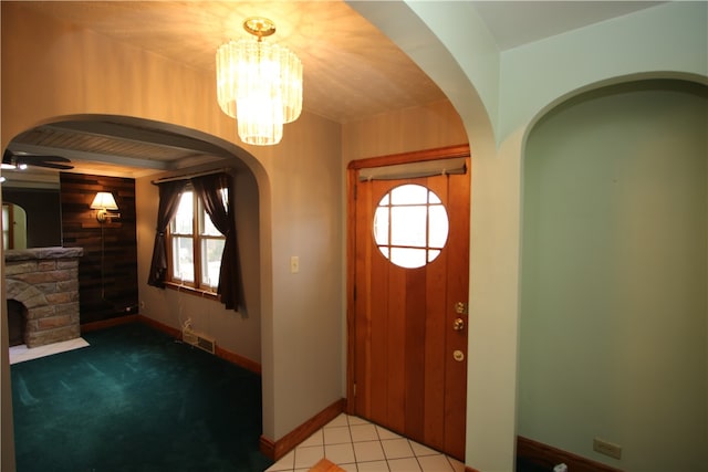 carpeted entryway featuring an inviting chandelier and a stone fireplace