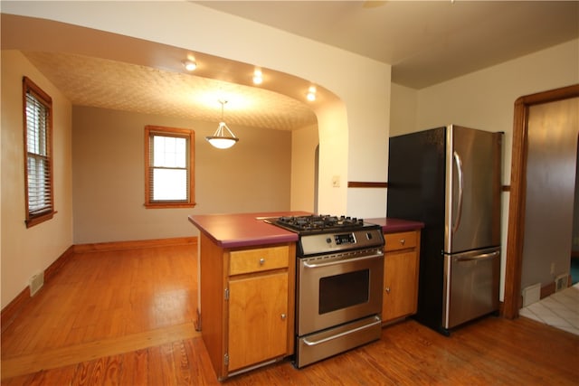 kitchen featuring kitchen peninsula, stainless steel appliances, hanging light fixtures, and light hardwood / wood-style flooring