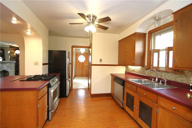 kitchen with appliances with stainless steel finishes, ceiling fan, sink, light hardwood / wood-style floors, and a stone fireplace