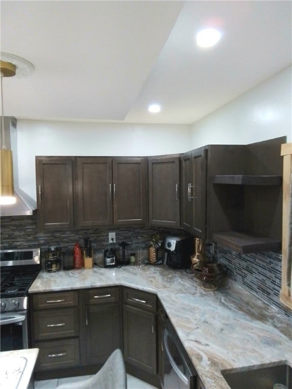 kitchen featuring wall chimney range hood, appliances with stainless steel finishes, tasteful backsplash, dark brown cabinets, and light stone counters