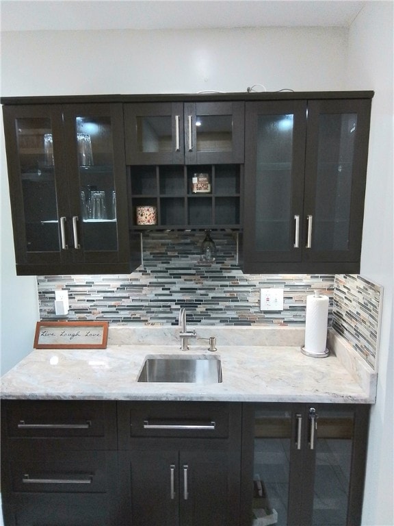 bar with tasteful backsplash, light stone counters, and sink