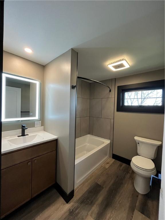 full bathroom featuring hardwood / wood-style flooring, tiled shower / bath combo, toilet, and vanity