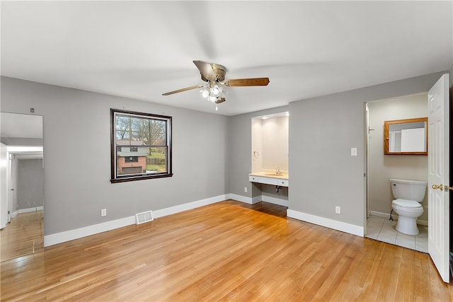 unfurnished bedroom with ceiling fan, light hardwood / wood-style floors, built in desk, and connected bathroom