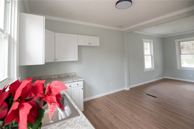 kitchen with sink, white cabinets, ornamental molding, and light wood-type flooring