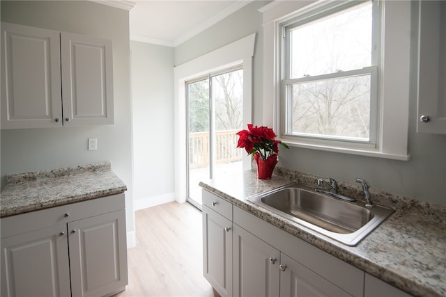 kitchen featuring light stone counters, crown molding, sink, light hardwood / wood-style floors, and white cabinetry