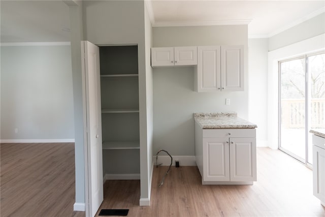 interior space featuring white cabinets, light stone countertops, light wood-type flooring, and crown molding