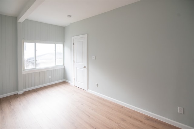 spare room featuring beamed ceiling, light hardwood / wood-style floors, and wood walls