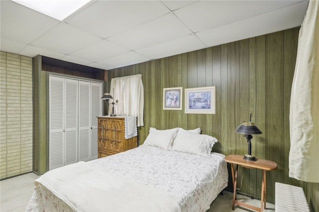 bedroom with a drop ceiling, a closet, and wooden walls