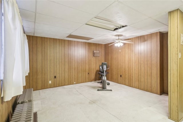 workout room with a drop ceiling, radiator heating unit, and wooden walls