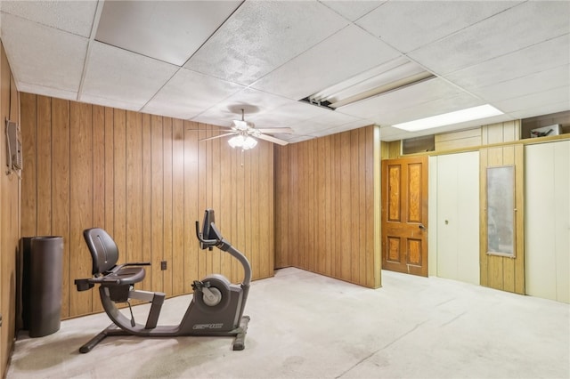 workout area featuring a drop ceiling, wood walls, light carpet, and ceiling fan