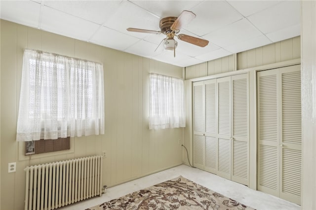 unfurnished bedroom with multiple windows, radiator heating unit, ceiling fan, and multiple closets