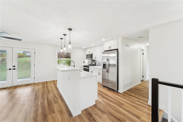 kitchen with hanging light fixtures, light hardwood / wood-style flooring, a center island with sink, white cabinets, and appliances with stainless steel finishes