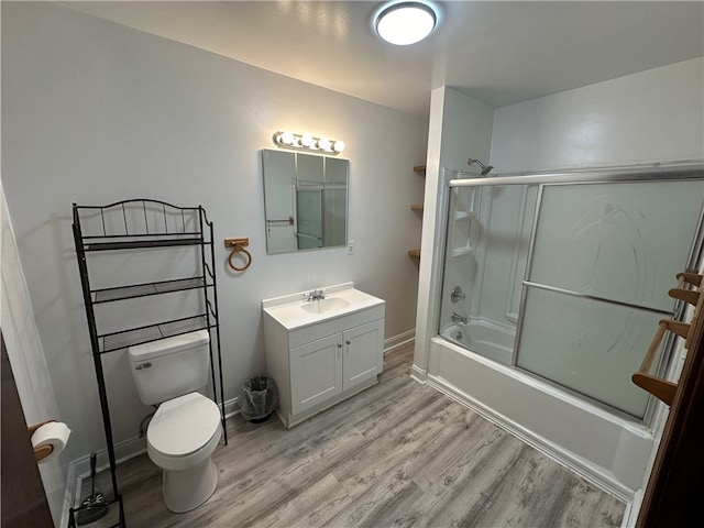 full bathroom with combined bath / shower with glass door, vanity, hardwood / wood-style flooring, and toilet