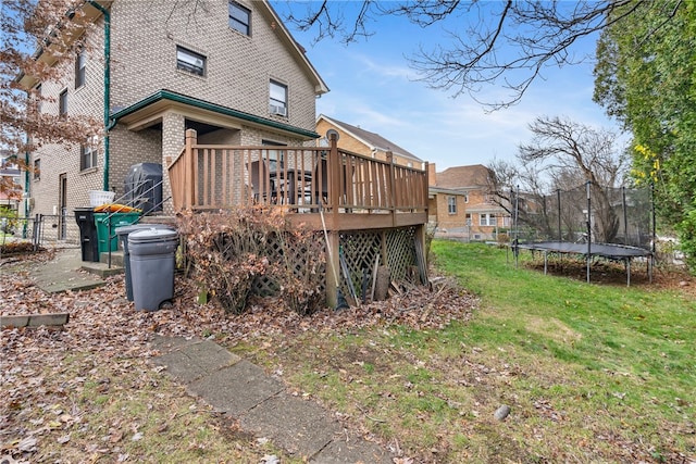 rear view of property with a deck, a trampoline, and a yard