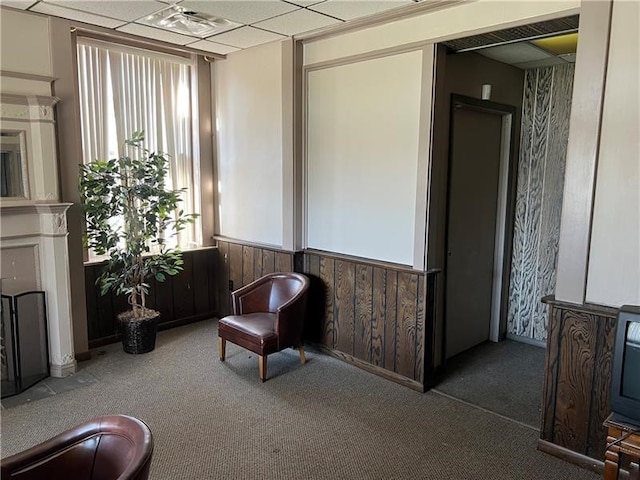 living area with carpet, a paneled ceiling, and wooden walls