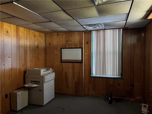 interior space with wood walls, a drop ceiling, and carpet floors