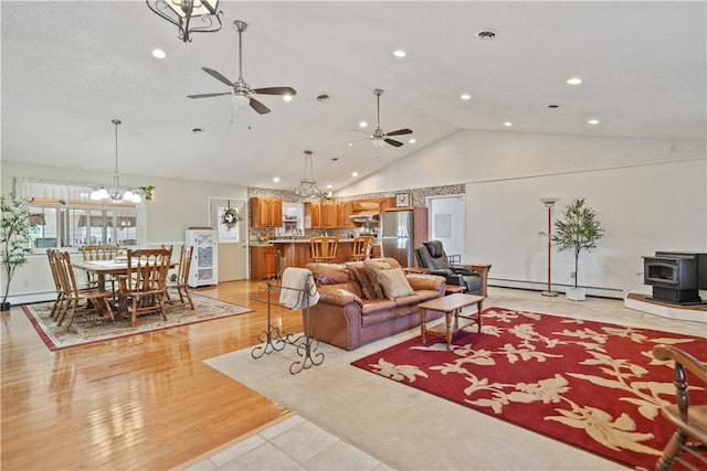 living room with light wood-type flooring, ceiling fan, a baseboard heating unit, a wood stove, and lofted ceiling