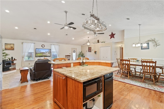 kitchen featuring light hardwood / wood-style floors, a wood stove, an island with sink, and black microwave