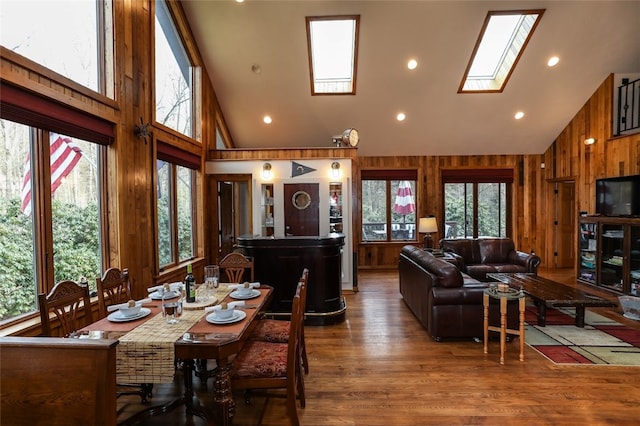 dining room with hardwood / wood-style floors, a skylight, high vaulted ceiling, and wood walls