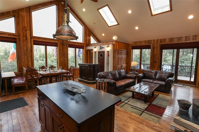 living room featuring wooden walls, a healthy amount of sunlight, high vaulted ceiling, and a skylight