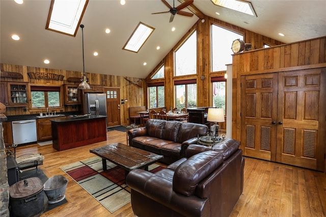 living room with light hardwood / wood-style floors, wood walls, a healthy amount of sunlight, and a skylight