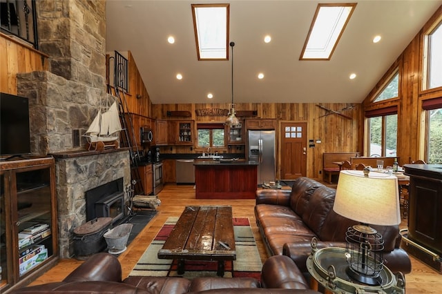 living room with a skylight, high vaulted ceiling, wooden walls, and light hardwood / wood-style flooring