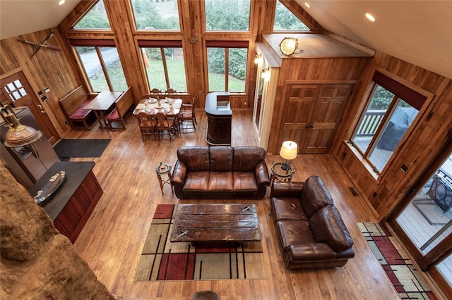 living room featuring wood walls, high vaulted ceiling, and light hardwood / wood-style flooring