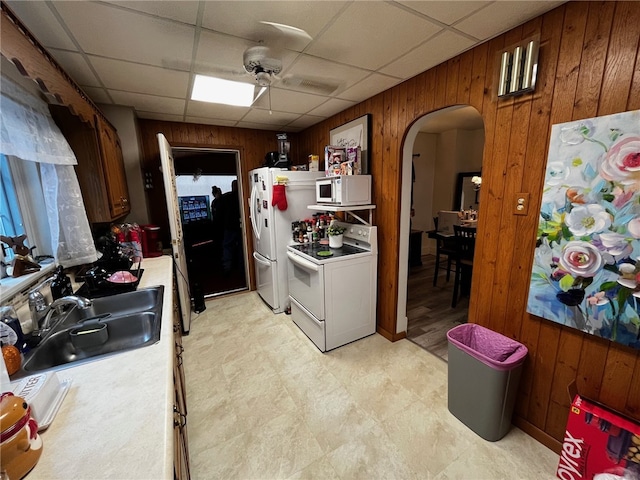 kitchen featuring a drop ceiling, white appliances, ceiling fan, sink, and wood walls