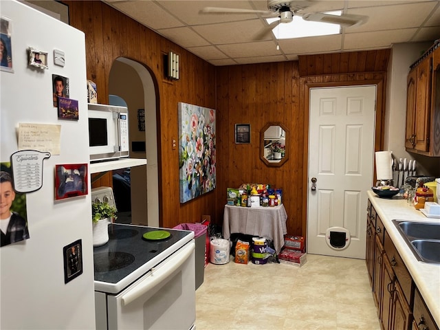 kitchen featuring ceiling fan, a drop ceiling, sink, wood walls, and white appliances