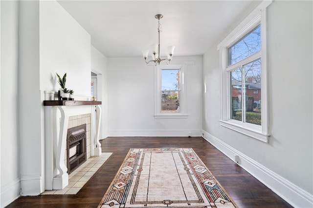 unfurnished dining area featuring a tile fireplace, wood-type flooring, and a notable chandelier