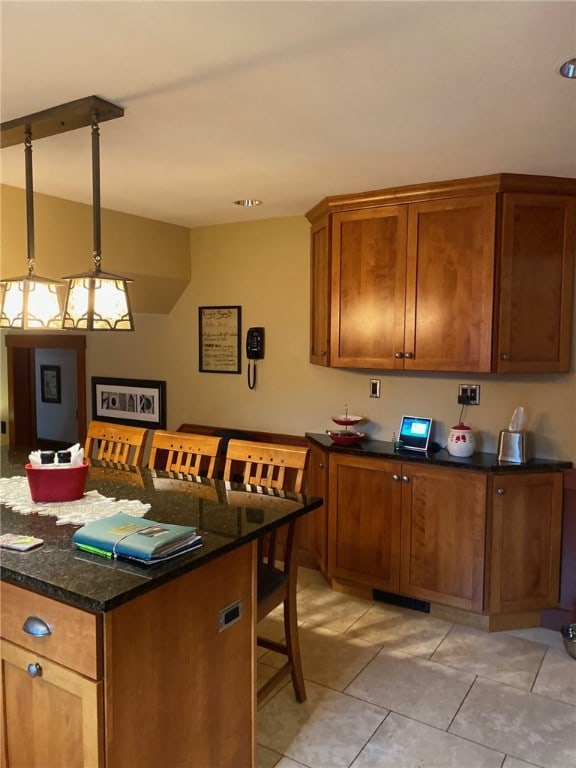 kitchen featuring a kitchen bar, dark stone countertops, light tile patterned floors, and decorative light fixtures