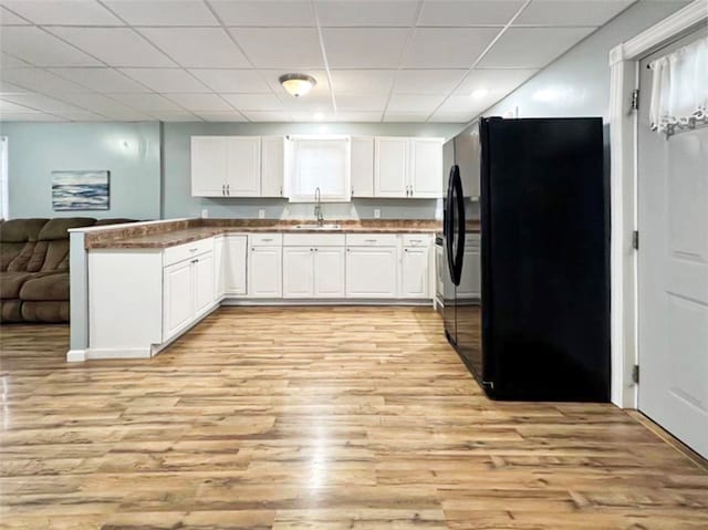 kitchen featuring a drop ceiling, white cabinets, black fridge, sink, and light hardwood / wood-style flooring