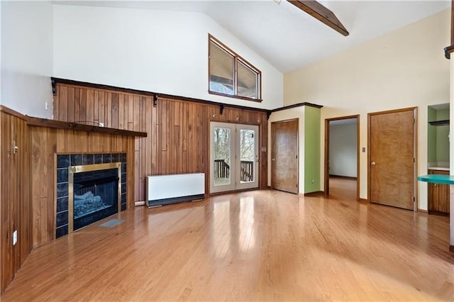 unfurnished living room featuring a tile fireplace, light hardwood / wood-style flooring, high vaulted ceiling, and wooden walls