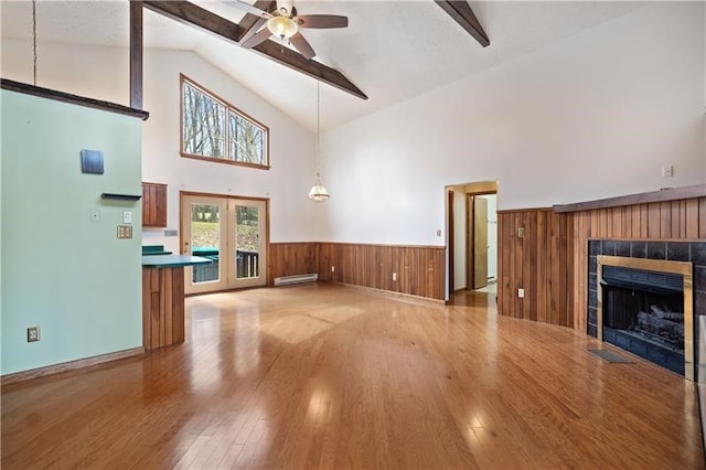 unfurnished living room with beam ceiling, ceiling fan, high vaulted ceiling, wood-type flooring, and a tiled fireplace