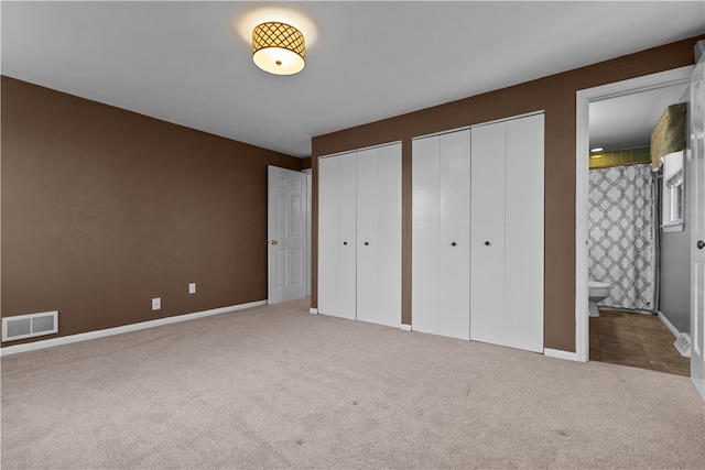 unfurnished bedroom with ensuite bath, carpet floors, and two closets