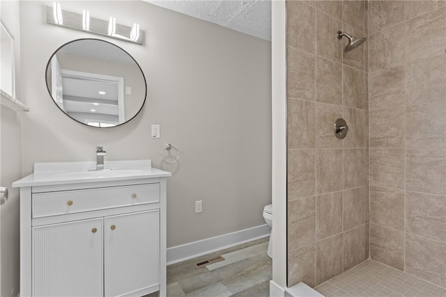 bathroom with a tile shower, vanity, a textured ceiling, and toilet