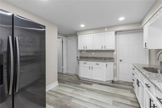 kitchen with white cabinets, sink, light hardwood / wood-style flooring, stainless steel fridge, and light stone counters