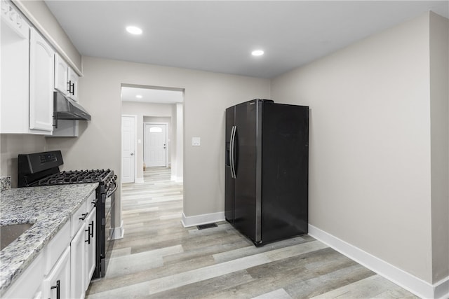 kitchen featuring light stone counters, white cabinets, black appliances, and light hardwood / wood-style floors