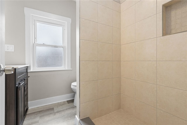 bathroom featuring wood-type flooring, vanity, a tile shower, and toilet