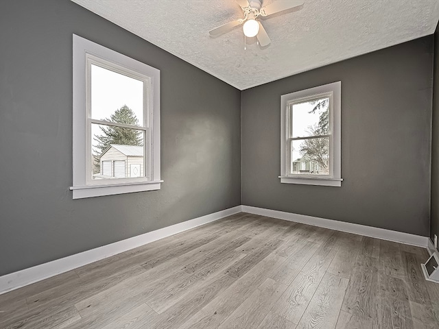 spare room featuring ceiling fan, a healthy amount of sunlight, a textured ceiling, and light wood-type flooring