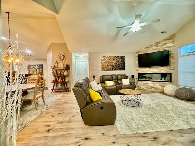 living room with a fireplace, vaulted ceiling, light hardwood / wood-style flooring, and ceiling fan with notable chandelier