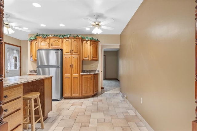 kitchen with a kitchen breakfast bar, stainless steel refrigerator, light stone counters, and ceiling fan